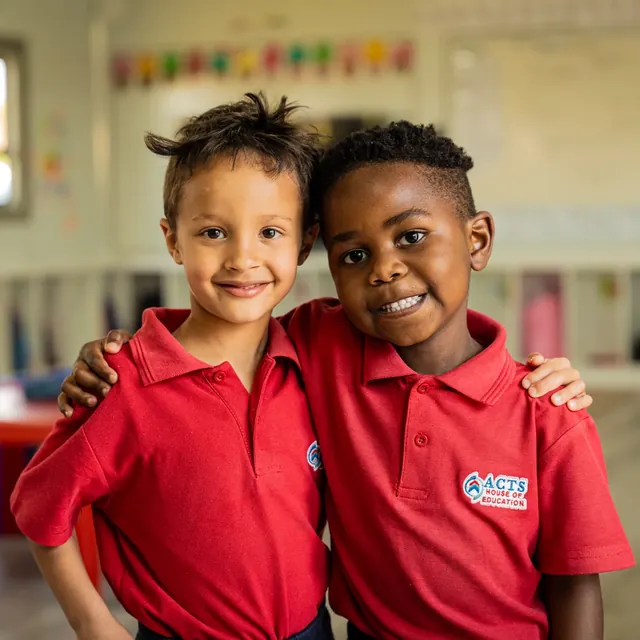 Two smiling Grade R learners in ACTS HOUSE OF EDUCATION shirts in their classroom