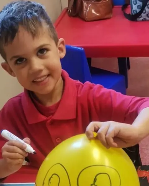 A boy smiling while he draws on a yellow balloon