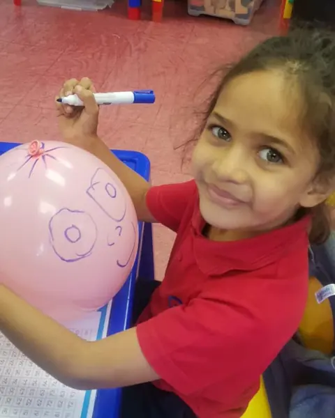 A girl drawing a face on a pink balloon with a marker