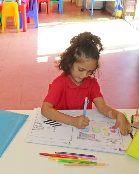 A girl colouring in a worksheet at her desk with coloured pencils