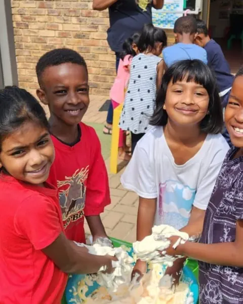 Grade R children laughing as they squish a messy play mix together outside